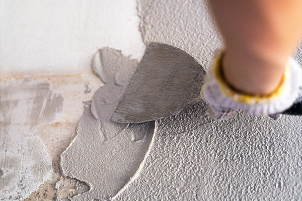 person using a spatula to apply plaster to a textured wall focusing on the smoothing technique for a perfect finish with five layers of plaster